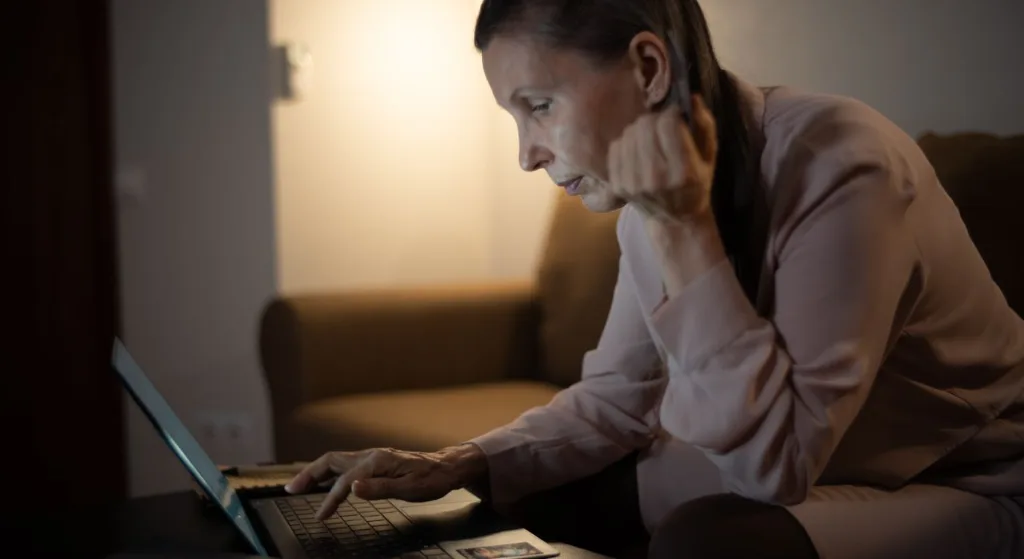 Senior woman using laptop in a dimly lit living room, focused on screen